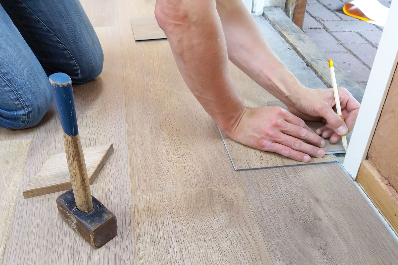 An installer measuring and marking a floor plank, hammer beside it.