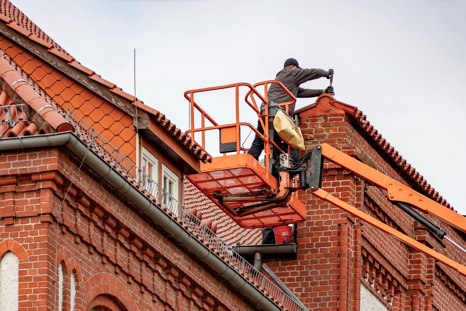 A worker in a lift basket working at the roofline of a brick building.