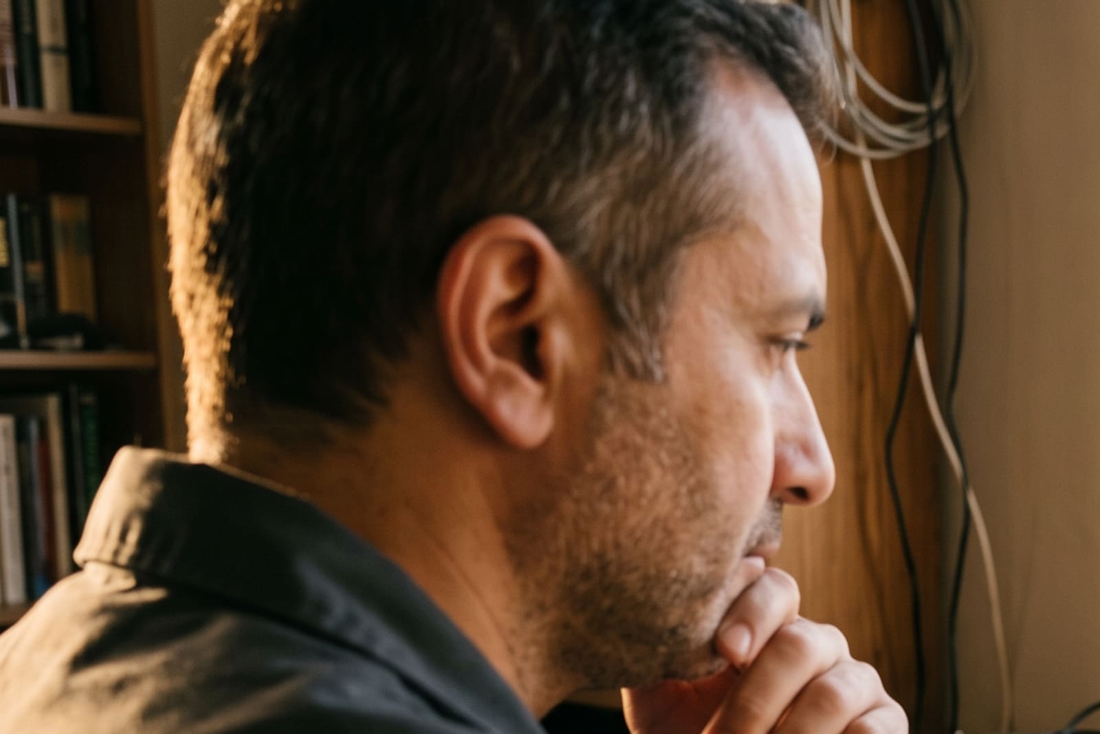 A generated image, not a real person: a business owner in a home office, chin in his hand, thinking hard as late sun comes through the window.