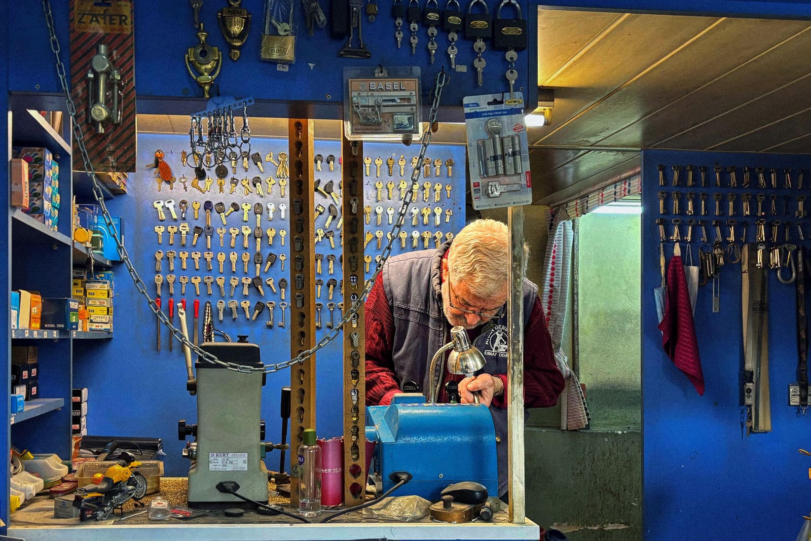 A locksmith working in his shop, walls of keys and locks behind him.