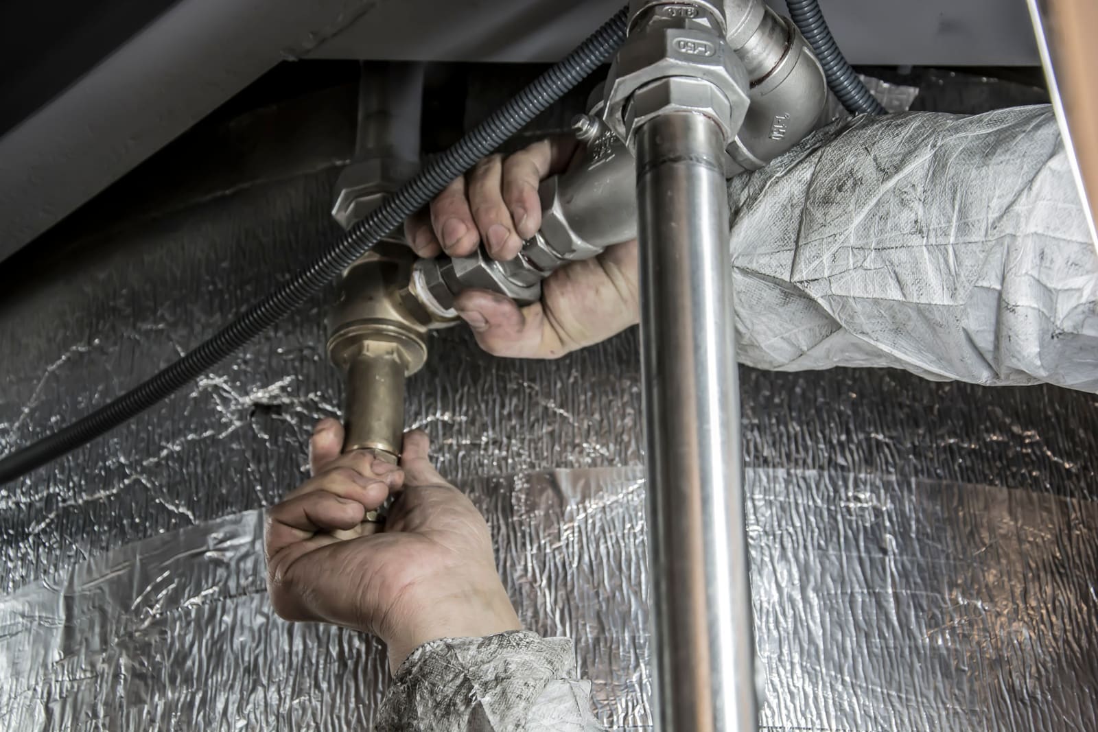 A plumber's hands fitting steel pipe and a valve.