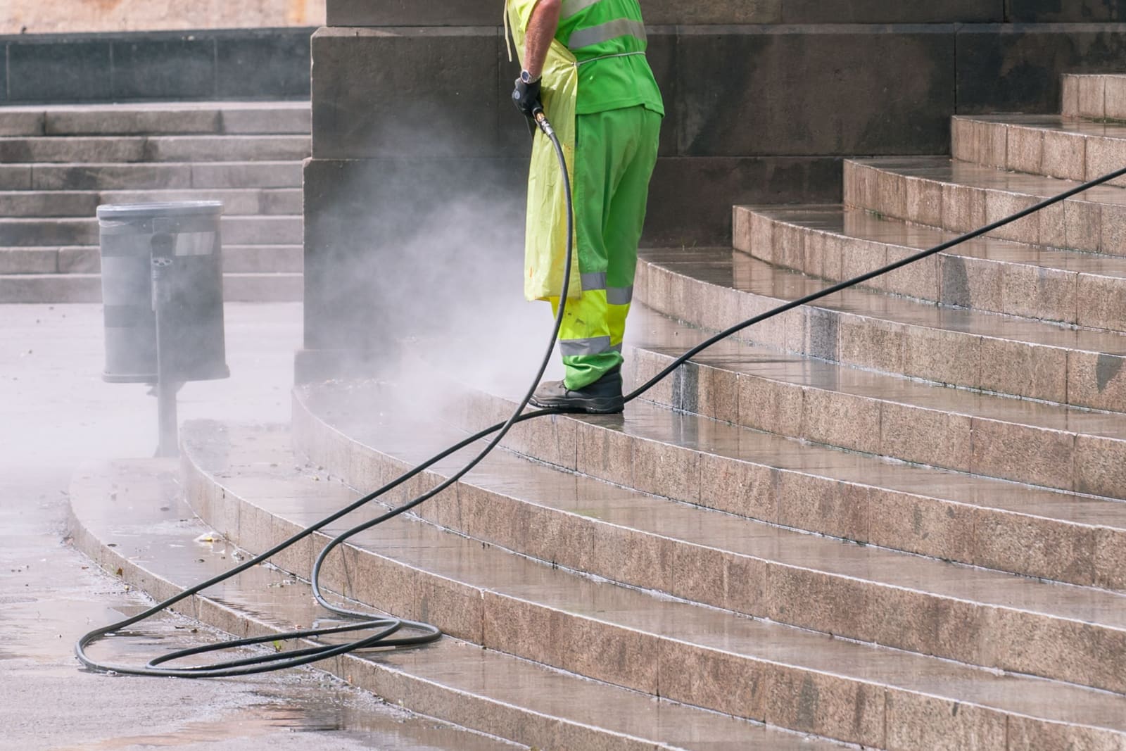 A worker in high-visibility clothes pressure washing stone stairs.