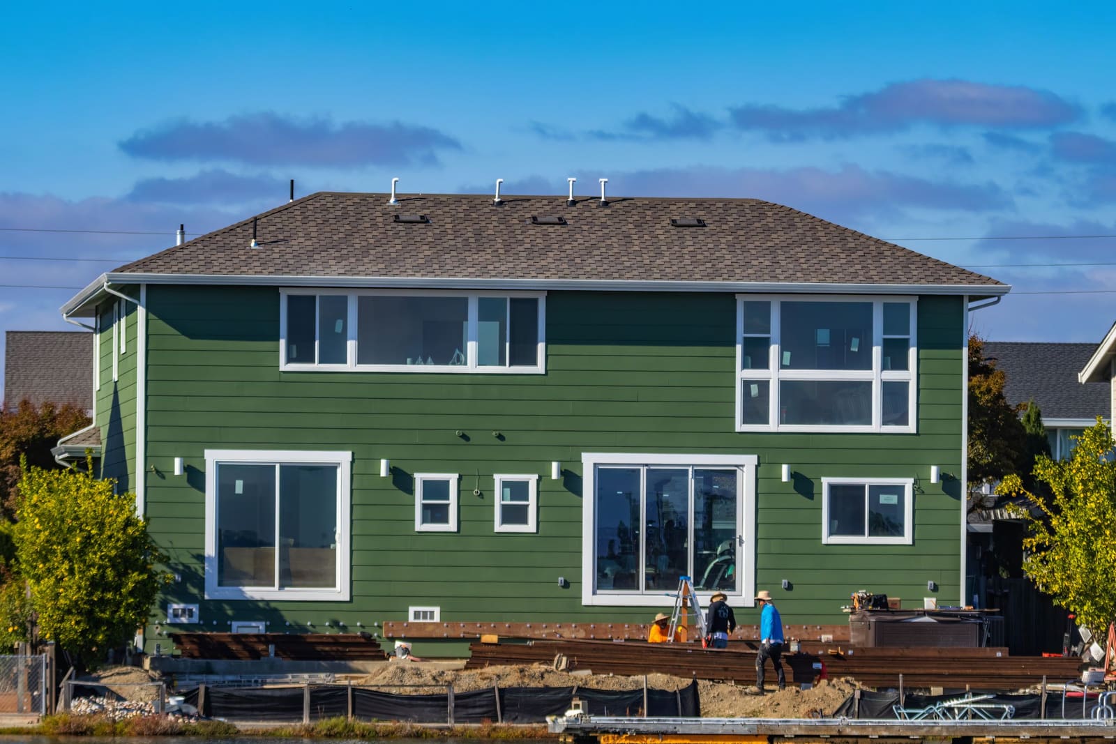 A house with new green siding, workers outside.