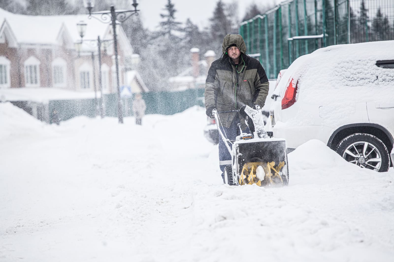 A man clearing a snowy street with a snow blower.